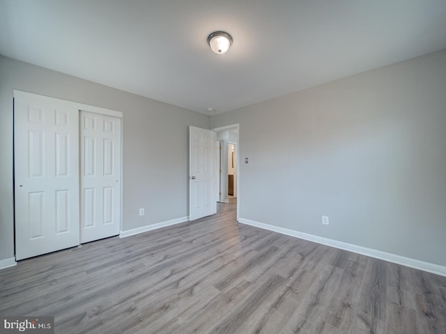 unfurnished bedroom featuring a closet, light wood-style flooring, and baseboards