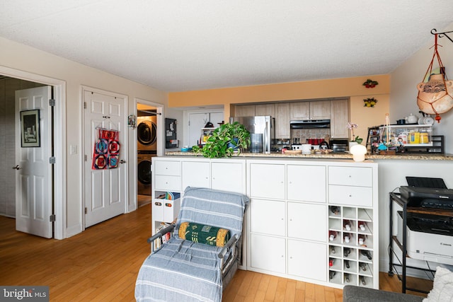 kitchen with stacked washer and dryer, decorative backsplash, light wood-style floors, freestanding refrigerator, and under cabinet range hood