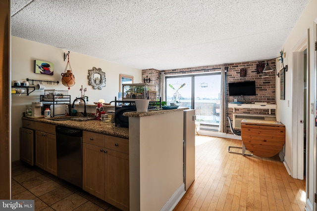 kitchen featuring a textured ceiling, a sink, black dishwasher, dark stone counters, and light wood finished floors