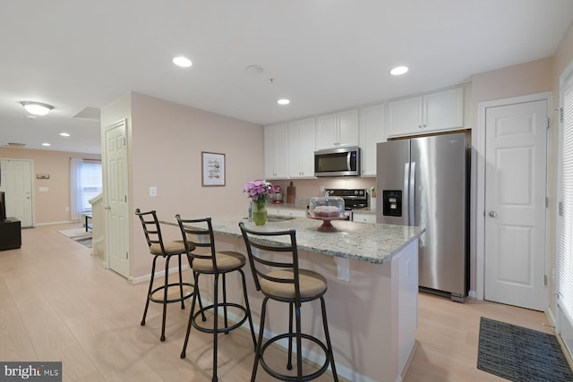 kitchen featuring a breakfast bar area, appliances with stainless steel finishes, white cabinetry, light stone counters, and light hardwood / wood-style floors