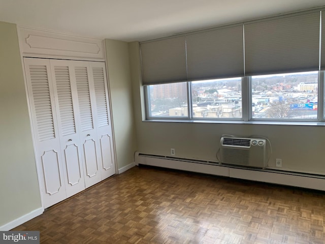 unfurnished bedroom featuring an AC wall unit, baseboard heating, a closet, and baseboards