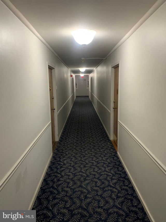 hallway featuring ornamental molding, dark colored carpet, and baseboards