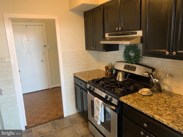 kitchen featuring exhaust hood, light stone counters, dark brown cabinets, and gas stove