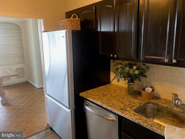 kitchen featuring light stone counters, stainless steel appliances, a sink, dark brown cabinets, and tasteful backsplash