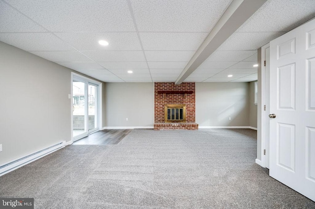 unfurnished living room with dark colored carpet, a brick fireplace, a baseboard heating unit, and a drop ceiling