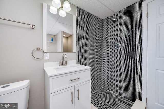 bathroom with vanity, a tile shower, a drop ceiling, and toilet