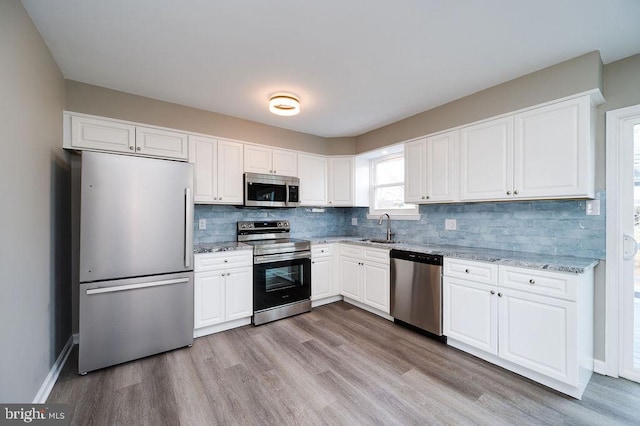 kitchen with sink, white cabinetry, appliances with stainless steel finishes, light stone countertops, and backsplash