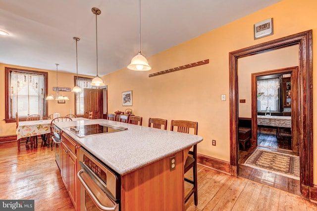 kitchen featuring hanging light fixtures, a center island, black electric stovetop, and light hardwood / wood-style flooring