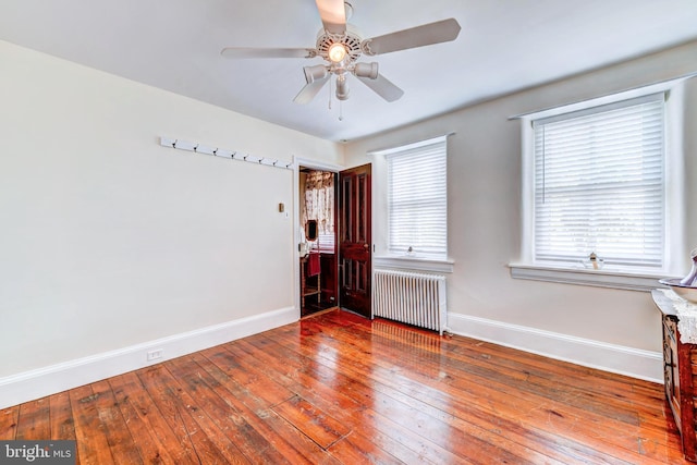 spare room featuring ceiling fan, wood-type flooring, radiator, and a wealth of natural light