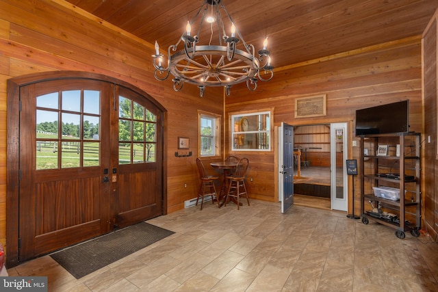 foyer entrance with wood walls, a notable chandelier, baseboard heating, wooden ceiling, and french doors