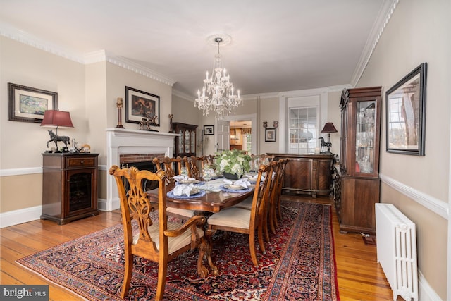 dining space with radiator, crown molding, a brick fireplace, and light wood-type flooring