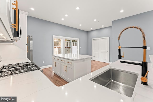 kitchen with white cabinetry, sink, range, light stone countertops, and light wood-type flooring