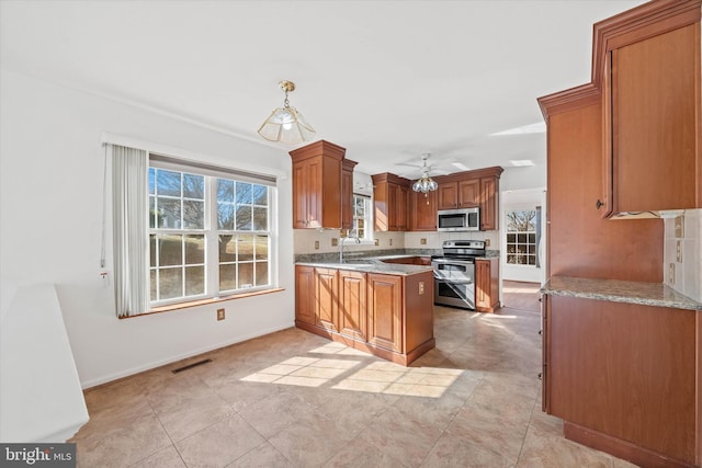 kitchen featuring sink, hanging light fixtures, stainless steel appliances, light stone countertops, and kitchen peninsula