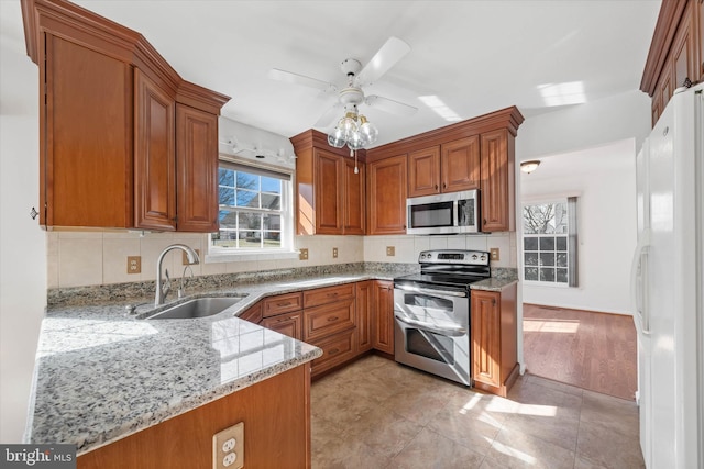 kitchen featuring sink, decorative backsplash, light stone counters, kitchen peninsula, and stainless steel appliances