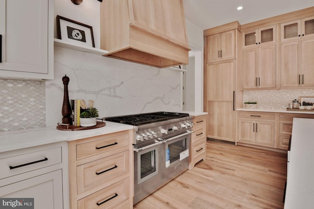 kitchen with light brown cabinets, double oven range, custom range hood, light hardwood / wood-style floors, and decorative backsplash