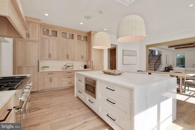 kitchen with stainless steel appliances, light stone counters, light hardwood / wood-style floors, a kitchen island, and decorative light fixtures