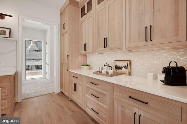 bar with light wood-type flooring, light stone counters, backsplash, and light brown cabinetry