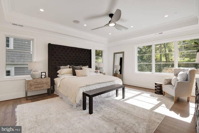 bedroom with a raised ceiling, crown molding, and light wood-type flooring