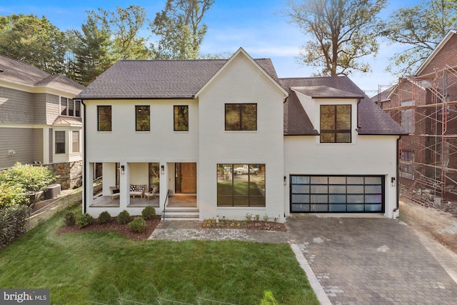 view of front of house with a garage, central AC, a front lawn, and covered porch