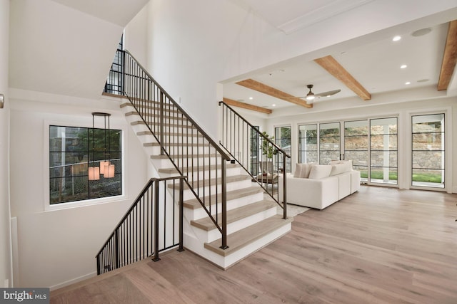 staircase featuring wood-type flooring, a towering ceiling, ceiling fan, and beam ceiling