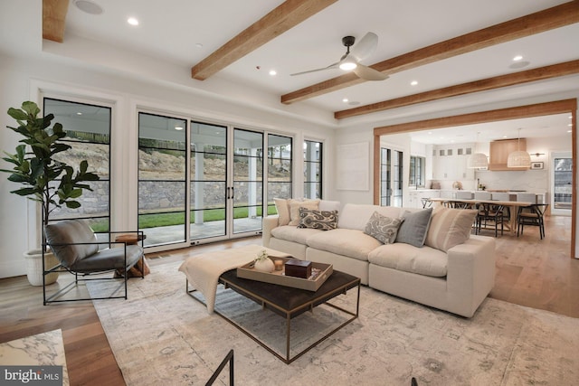 living room featuring beamed ceiling, ceiling fan, and light wood-type flooring