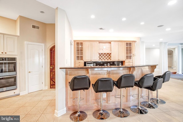 7024 Green Oak Dr, Mclean, VA 22101 - kitchen with arched walkways, a breakfast bar area, glass insert cabinets, light tile patterned floors, and recessed lighting