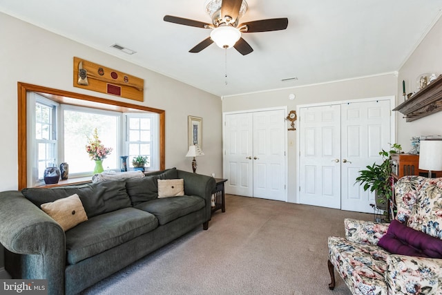 living area with a ceiling fan, crown molding, visible vents, and carpet flooring