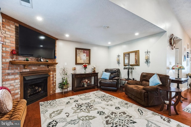 living area with a brick fireplace, visible vents, a textured ceiling, and wood finished floors