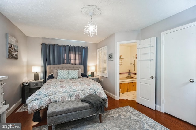 bedroom featuring baseboards, wood finished floors, ensuite bathroom, an inviting chandelier, and a textured ceiling