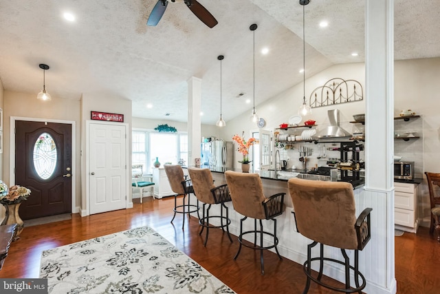 kitchen with wall chimney exhaust hood, dark wood-style flooring, dark countertops, and a kitchen breakfast bar