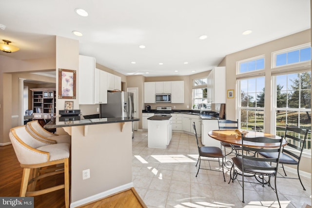 kitchen with a breakfast bar area, stainless steel appliances, a peninsula, white cabinets, and dark countertops