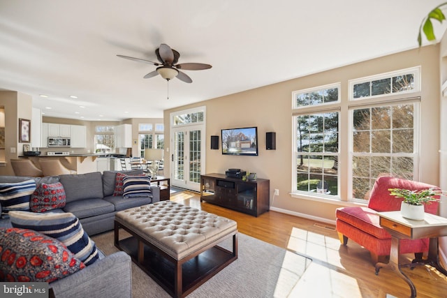 living area featuring a ceiling fan, french doors, a healthy amount of sunlight, and light wood-style flooring