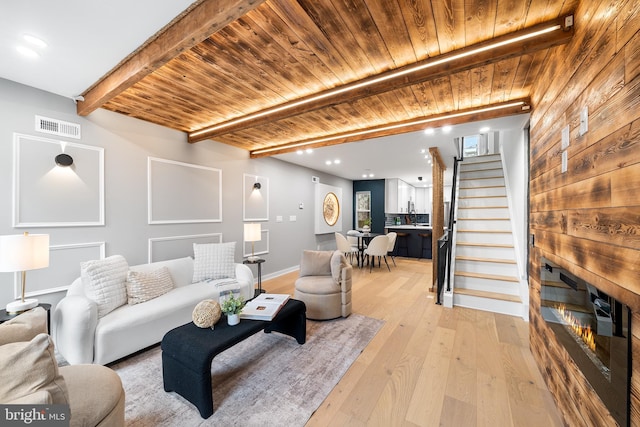 living room featuring a fireplace, beam ceiling, light hardwood / wood-style flooring, and wooden ceiling