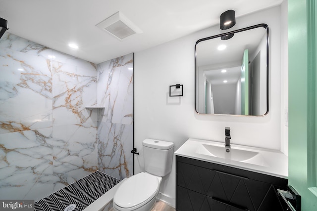 bathroom featuring vanity, a tile shower, and toilet