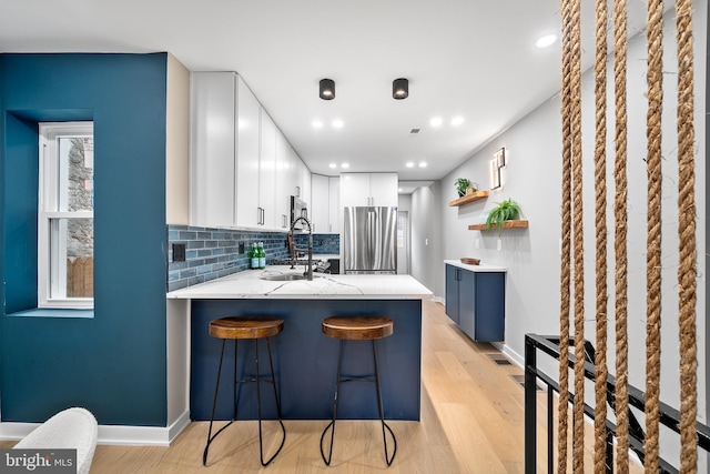 kitchen featuring stainless steel fridge, white cabinetry, a kitchen breakfast bar, decorative backsplash, and kitchen peninsula