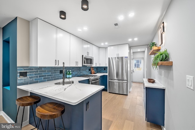 kitchen with appliances with stainless steel finishes, white cabinetry, sink, a kitchen breakfast bar, and kitchen peninsula