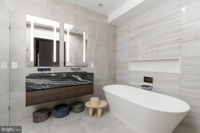 full bathroom featuring a freestanding bath, tile walls, and vanity