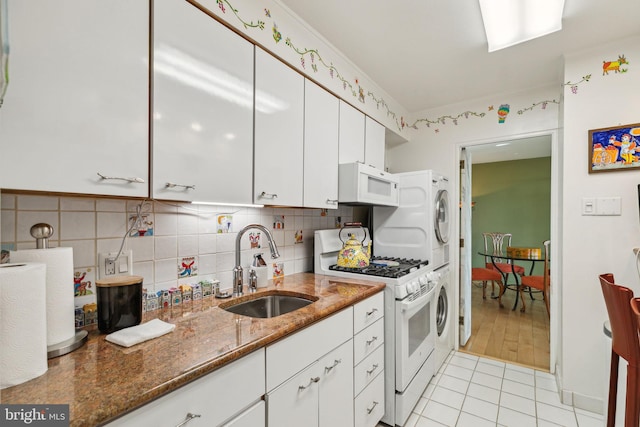 kitchen with sink, white appliances, dark stone countertops, stacked washer / dryer, and white cabinets