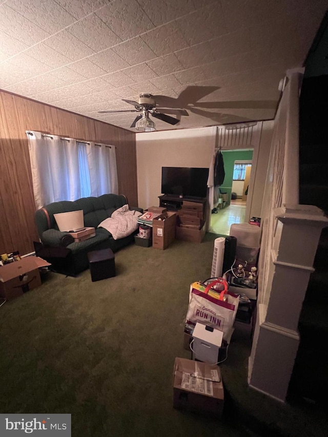 carpeted living room with ceiling fan and wood walls