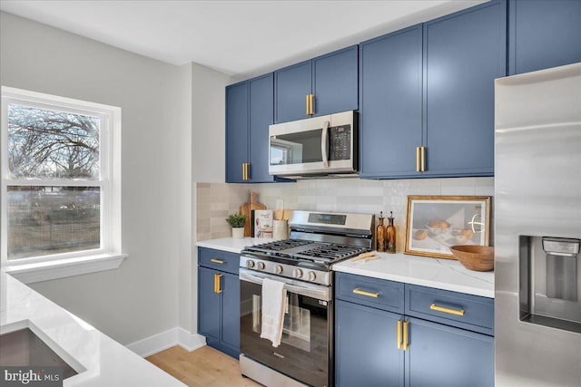 kitchen with blue cabinets, backsplash, light hardwood / wood-style floors, and appliances with stainless steel finishes