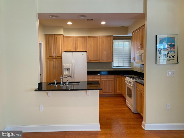 kitchen featuring a breakfast bar, sink, hardwood / wood-style flooring, kitchen peninsula, and white appliances