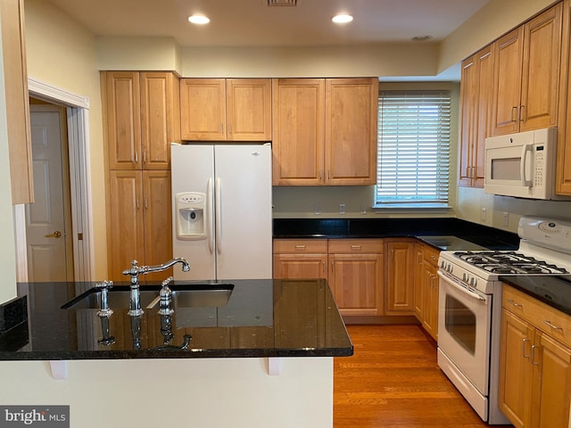 kitchen featuring sink, white appliances, hardwood / wood-style flooring, dark stone countertops, and a kitchen breakfast bar