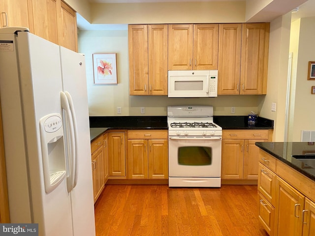 kitchen with dark stone countertops, white appliances, and light hardwood / wood-style flooring