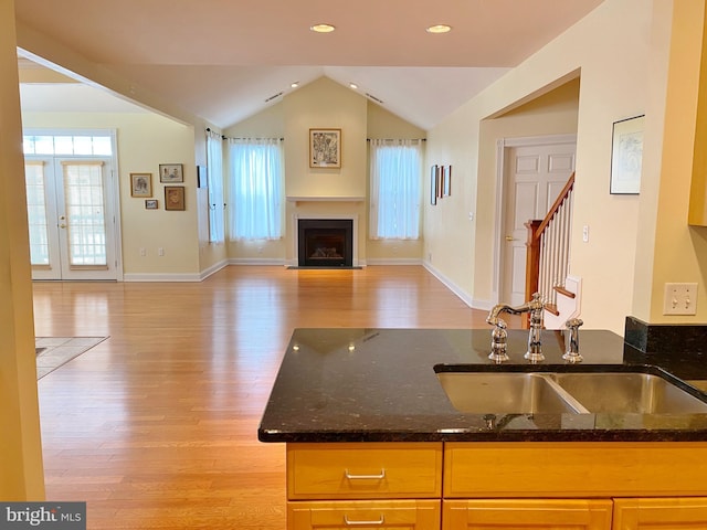 kitchen with lofted ceiling, dark stone counters, light hardwood / wood-style floors, and sink