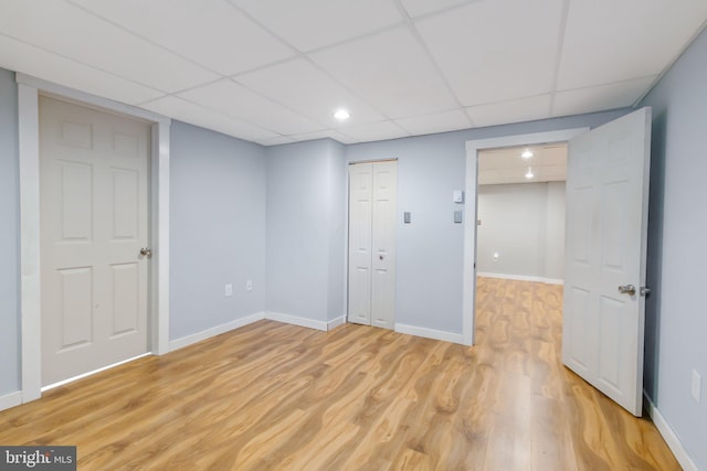 spare room with light wood finished floors, a paneled ceiling, and baseboards