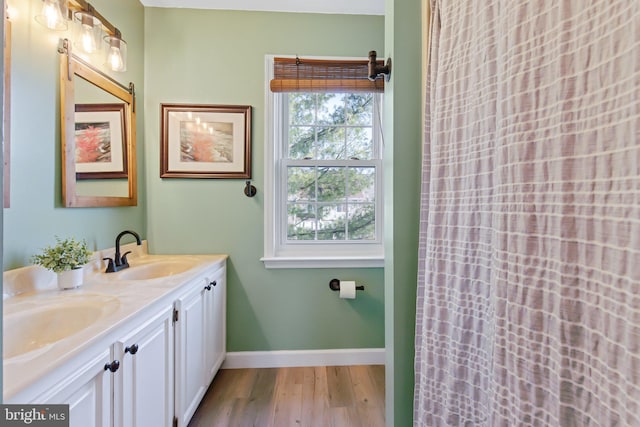 bathroom featuring a sink, baseboards, wood finished floors, and double vanity