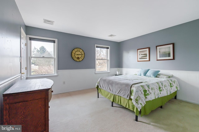 carpeted bedroom featuring a wainscoted wall and visible vents