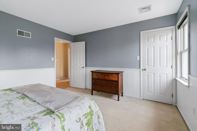 carpeted bedroom with visible vents, wainscoting, and multiple windows