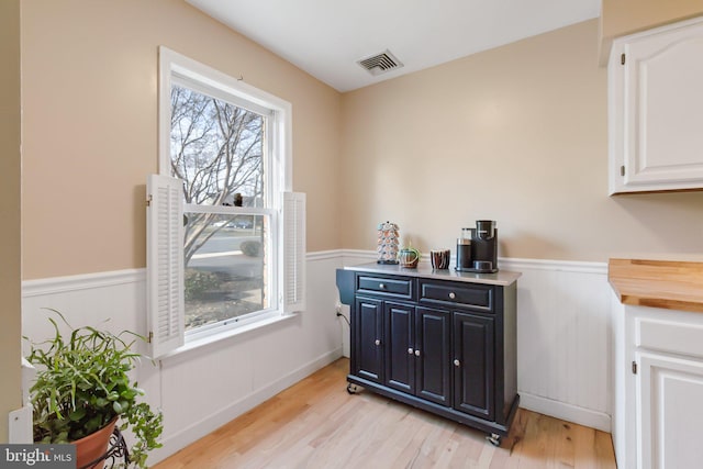 interior space with light wood-type flooring, visible vents, and wainscoting