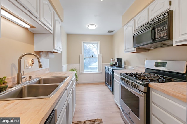 kitchen featuring stainless steel gas range oven, visible vents, black microwave, butcher block countertops, and a sink